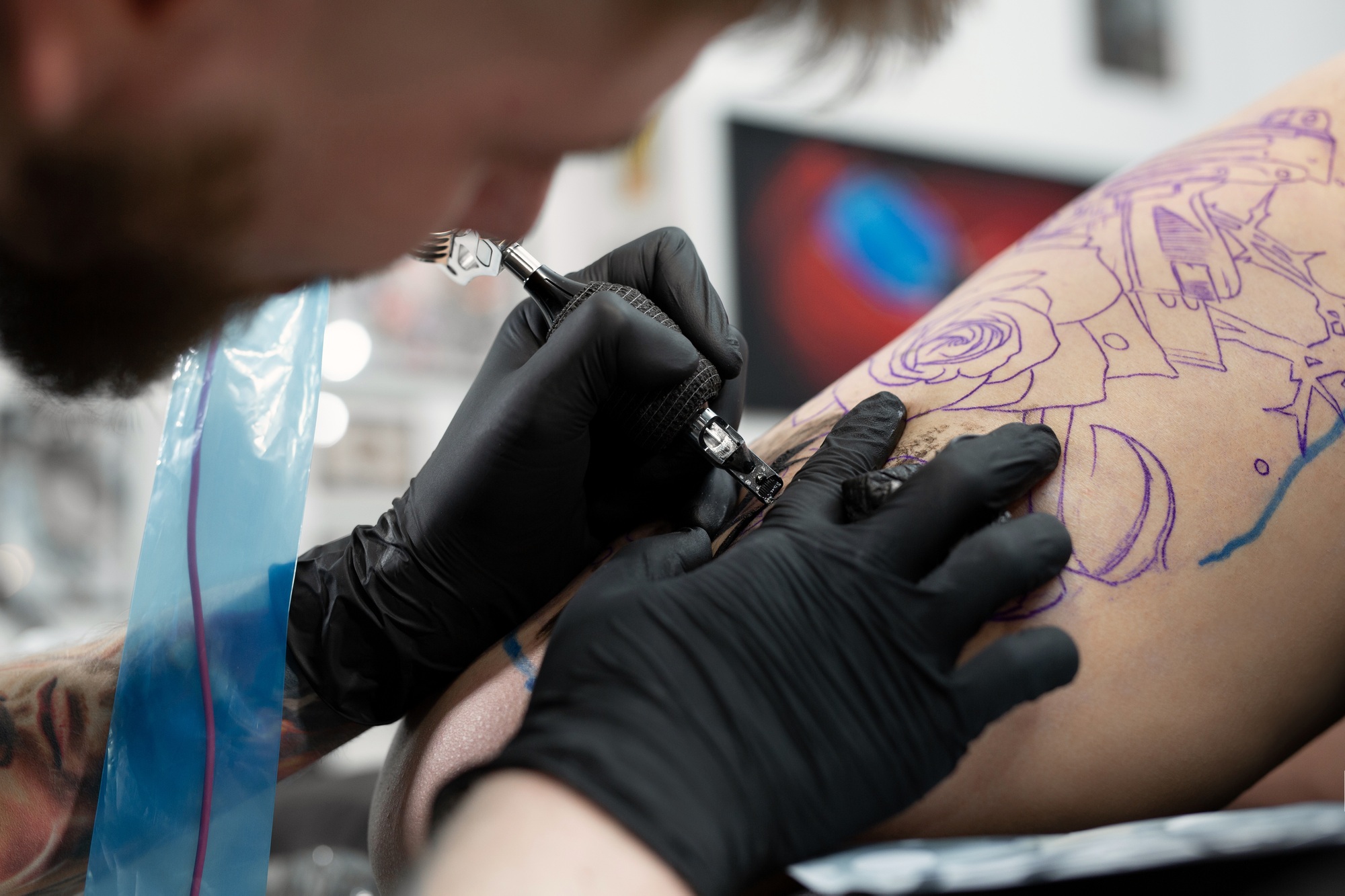 Close up image of the bearded tattoo male artist makes a tattoo on a female leg.