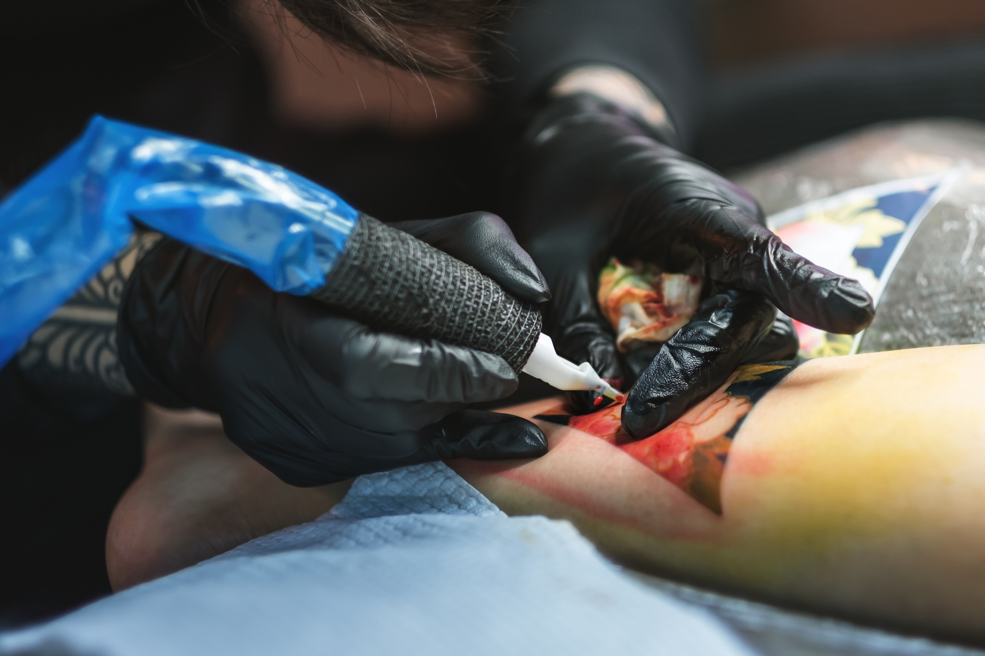 Tattoo artist inserting colored ink in human skin with electric tattoo machine