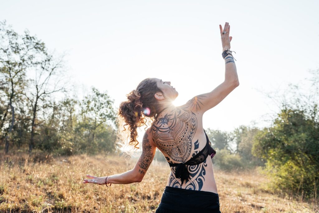 Tribal Dancer Poses With Tattooed Back Against Sunlight in Natural Setting