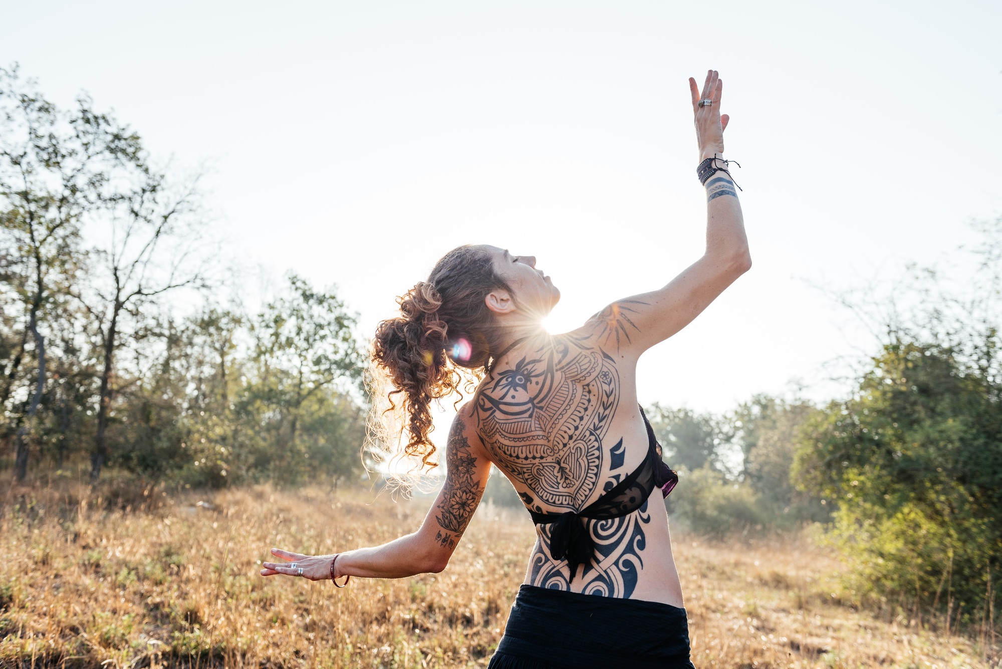Tribal Dancer Poses With Tattooed Back Against Sunlight in Natural Setting